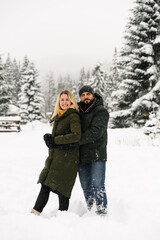 Attractive man and woman cuddling in the frosty forest. Adult couple in puffer jacket have fun on walk. Romantic date in winter time.Winter lovestory