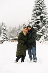 Fototapeta na wymiar Attractive man and woman cuddling in the frosty forest. Adult couple in puffer jacket have fun on walk. Romantic date in winter time.Winter lovestory