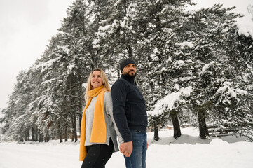 Attractive man and woman cuddling in the frosty forest. Adult couple in sweaters have fun on walk. Romantic date in winter time.Winter lovestory