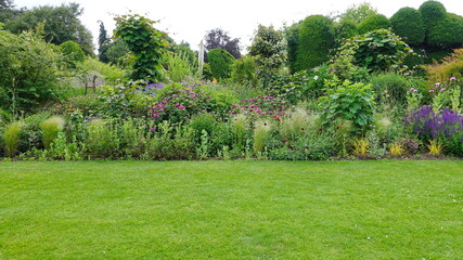 Fototapeta na wymiar Scenic View of a Beautiful English Style Landscape Garden with a Green Mowed Lawn, Colourful Flower Bed and Leafy Trees