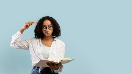 Thoughtful young black female student reading book, thinking over something on blue background,...
