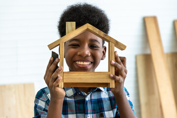 Portrait of smiling African black boy child kid carpenter holding a model of wooden house in carpentry workshop. Concept hobby at home. - obrazy, fototapety, plakaty