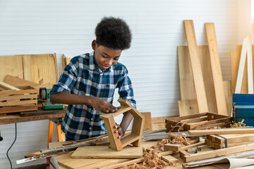 African black boy child kid carpenter sanding wood with sandpaper in carpentry workshop. Concept hobby at home. - obrazy, fototapety, plakaty