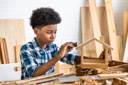 African black boy child kid carpenter sanding wood with sandpaper in carpentry workshop. Concept hobby at home.