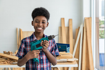 Portrait of African black boy child kid carpenter holding electric drill in carpentry workshop. Concept hobby at home.