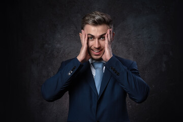 Fototapeta premium Young businessman man scared in a state of anxiety and daze holding his head with his hands on a dark background.