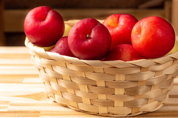 Plums, beautiful and juicy plums in a straw basket positioned on a rustic wooden surface, selective focus.