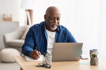 Senior Black Man Using Laptop Taking Notes Working At Home