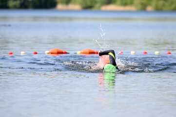 Swimmer swimming outdoor in nature with a green swimming cap and orange buoy