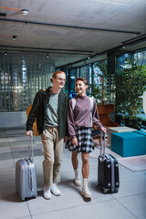 Positive couple with baggage walking in hotel lobby