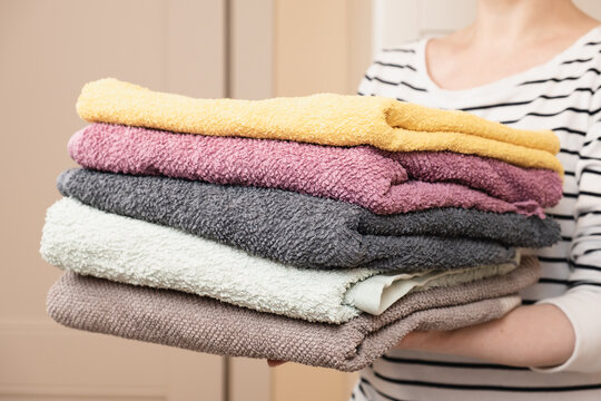 Woman Holds A Stack Of Clean Terry Towels. Folding Clean Linen, Cleaning The House, Caring For Home Textiles. Taking Care Of The Family.