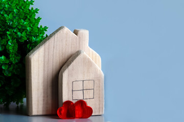 Two wooden houses on blue background with green plant and two red hearts. Concept of love in house,...