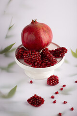 A serene still life capturing the essence of pomegranates, with their vibrant seeds spilling over, all set against a gentle backdrop adorned with subtle foliage.