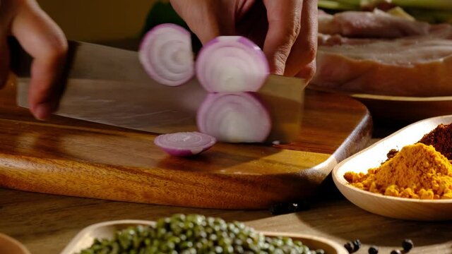 A Motion of chef cutting a onion in a wooden chopping board and ingredient in kitchen background