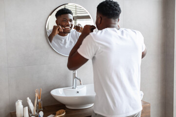 African guy using tooth floss caring for teeth in bathroom
