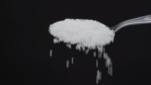Pouring sea salt from an iron tablespoon on a black background close-up. For cooking food. In slow motion.