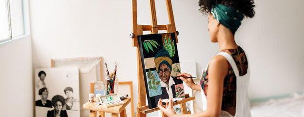 Young female painter working on a portrait painting in her studi - obrazy, fototapety, plakaty