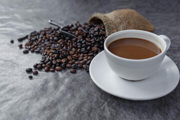 A cup of coffee and roasted coffee beans in a brown bag.