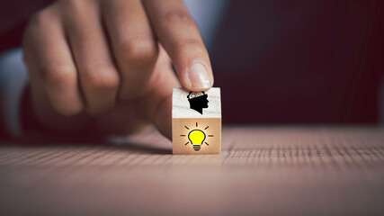 Problem solving, new ideas, creativity, teamwork, and innovation concepts. Person hand flips one wooden cubes block one revealing an idea light bulb icon, head symbols.