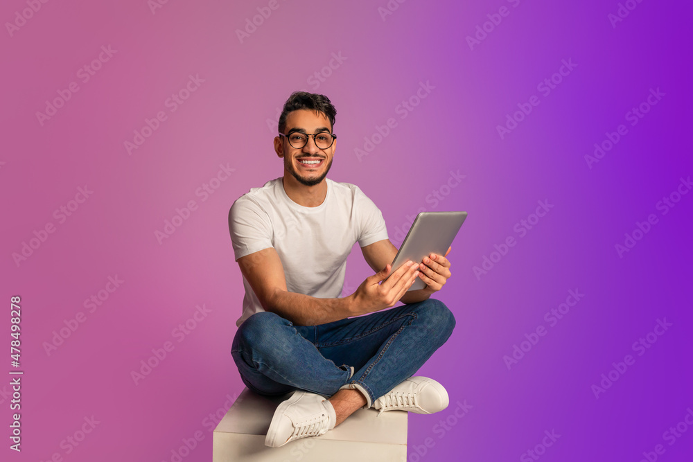 Poster full length of young arab man using digital tablet, checking new app in neon light