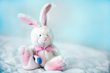 Toy Hare wearing protective medical mask with contactless infrared thermometer at forehead. Measuring high temperature of children with influenza and viruses, coronavirus. 