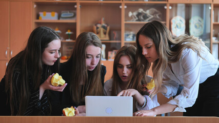 Schoolchildren friends working together in class with a laptop and eating apples.