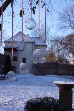Inspiring details, decor garden: outdoor hanging glass transparent candle sphere balls, pink ribbons tree branch. Krakow park Decjusza. Pure frosty shades of winter. Beauty at low temperatures is real
