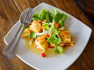 Yam khai dao fried egg spicy sour salad with vegetables and herbs is a Thai dish close up in the plate on wooden table. Top view from above