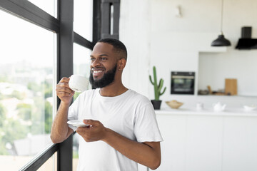 Smiling African American man drinking coffee looking through window