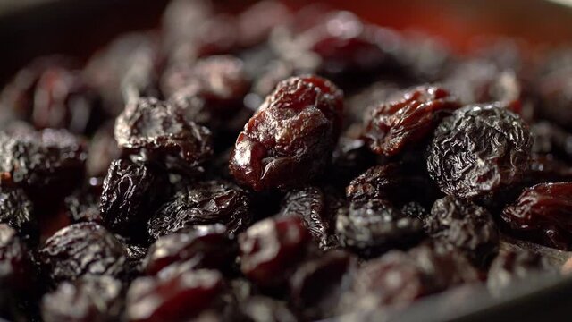 Close up macro view of Black dry grape raisins, moving food texture. Concept of healthy and organic food. Dried fruits snacks on red bowl.