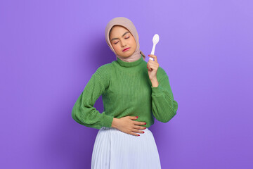 Hungry beautiful Asian woman in green sweater and hijab holding a spoon and think of tasty food...