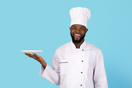 Portrait Of Smiling Young Black Chef In Uniform Holding Empty Plate