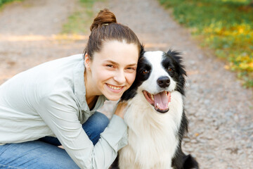 Naklejka na ściany i meble Smiling young attractive woman playing with cute puppy dog border collie on summer outdoor background. Girl holding embracing hugging dog friend. Pet care and animals concept.