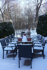 Winter time inspiring details of the urban landscape.Close empty cafe terrace, outdoor furniture table with chairs covered with fresh snow, sleeping flower plant in pots. Krakow, city park Decjusza.