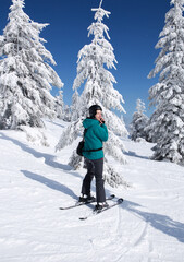 Fototapeta na wymiar happy woman in a ski suit, helmet, stands in the mountains against the background of ice trees on a sunny winter day. a minute of rest, relaxation, pleasure, winter holidays. love winter