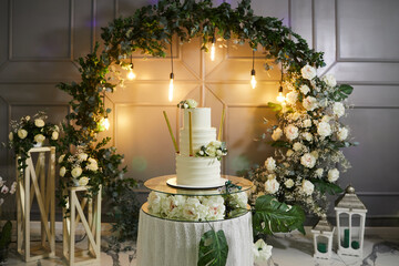 Beautiful white three tier cake with fresh flowers with incandescent lamps, fresh flowers and white lanterns in the background. 