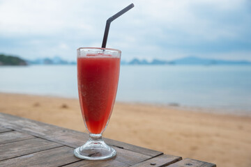 A glass of tasty watermelon juice on the wooden table on the beach.
