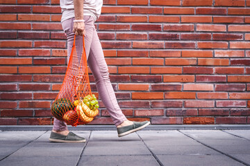 Woman walking with reusable mesh bag full of fruits. Sustainable lifestyle, plastic free shopping...