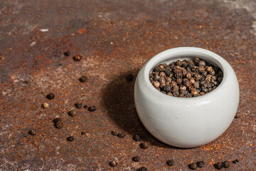 Dried black peppercorns in a ceramic bowl. Rusty metal background. Trendy hard light, dark shadow