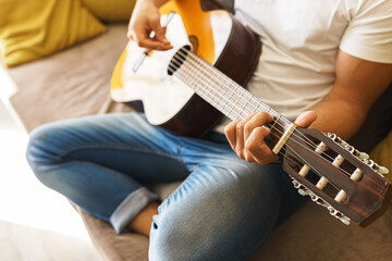 Young man on sofa is playing acoustic guitar