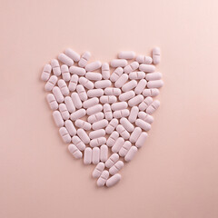 Heart made of pills on pink background. Creative concept for Valentine's Day or Pharmacy, Dietary Supplement and Cardio Medicines.