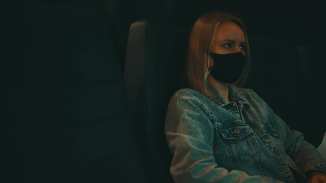 Woman in medical mask is watching movie in the cinema.