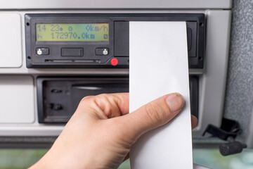 Close up of a driver holding empty printed day shift in focus against a digital tachograph out of...