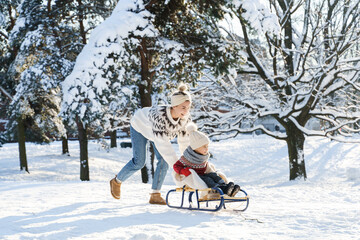 Mother and her cute little son having on a sledding hill during sunny winter day