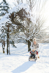Fototapeta na wymiar Mother and her cute little son having on a sledding hill during sunny winter day