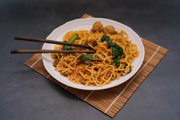 Fried noodles with chicken meatballs served with chopsticks on a white plate with a black background