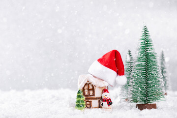 Santa Claus Hat on Country house over silver background with New Year spruce trees on snow