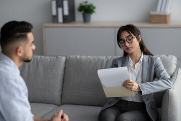 Psychotherapy concept. Focused female psychotherapist interviewing young man, listening and taking notes