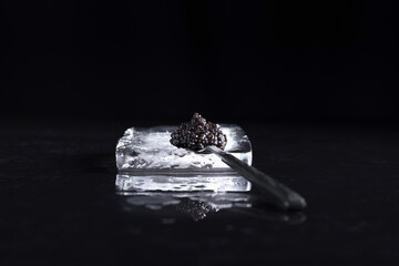 Caviar negro de esturión en una cuchara, sobre una piedra de hielo reflejada en fondo negro. Comida delicatessen de lujo