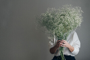 woman holding white gypsophila blooming flowers, hiding behind bouquet